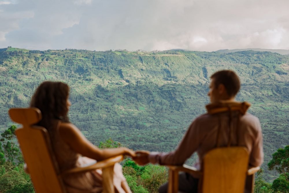 Pareja sentada en mecedoras agarrados de la mano, mirando hacia el Valle de Tenza desde el Chalet de Paja.