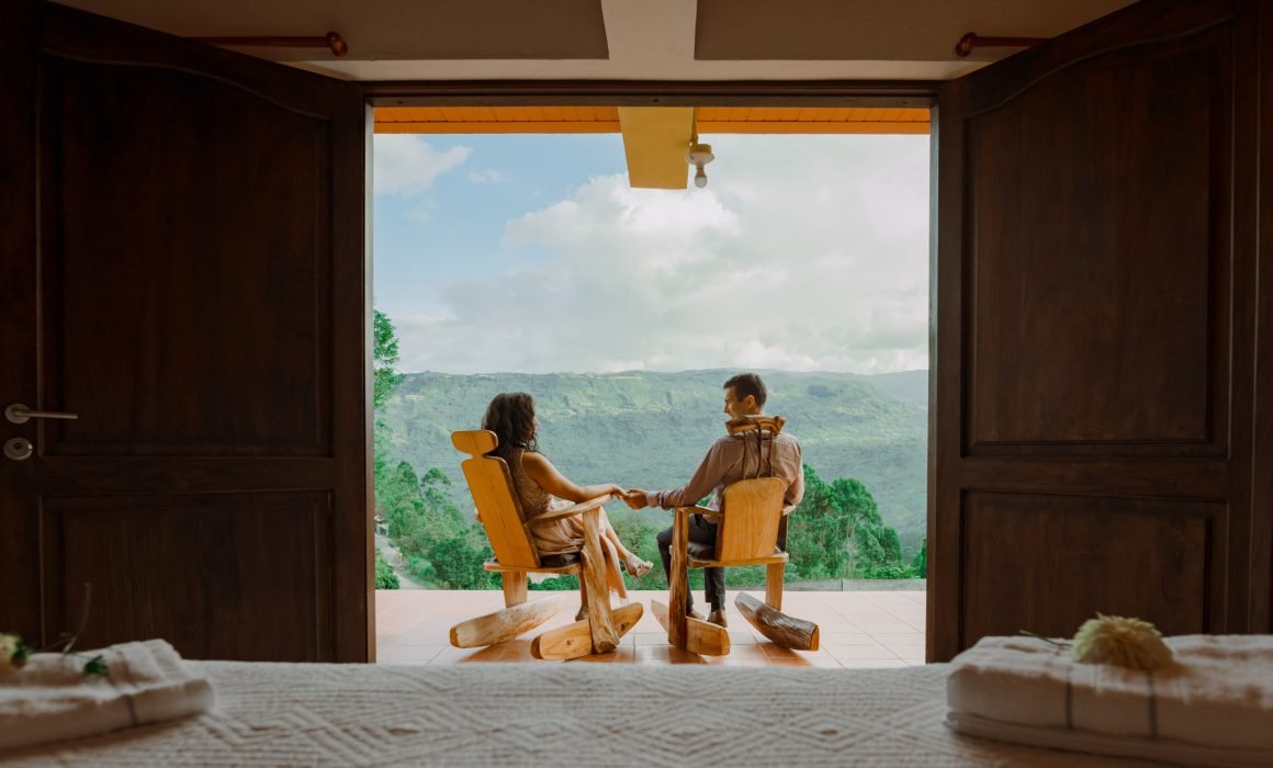 Pareja agarrada de manos sentados en dos mecedoras demadera con vista hacia el Valle de Tenza en Guateque, Boyacá.